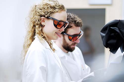 two scientists in white coats and goggles work in a lab