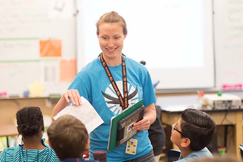 teacher handing papers to students in elementary classroom