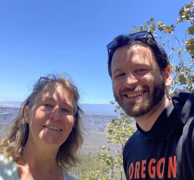 An OSU student and a scientist stand together and smile for the camera. In the background is a rocky landscape and bright blue sky.