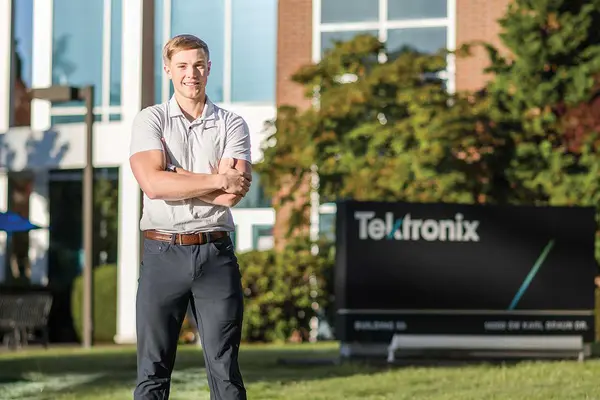 Wyatt Weaver, wearing a business polo and slacks, poses in front of an office building