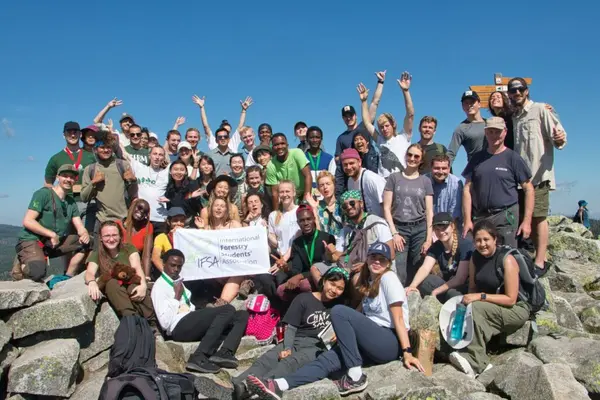 A group of forestry students pose with a banner for their student association on a rocky mountaintop.